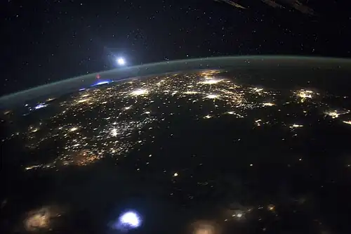 A sprite at the horizon, with lightning below in the troposphere and above the green line of airglow at the upper mesopause and border to space (the bright light above is the Moon).