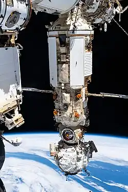 A photograph of two modules, one large and one small, attached to a space station with the Earth visible underneath