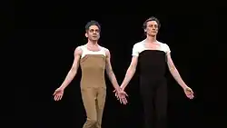 Two dancers, Ferver and Bartelme, face forward wearing chest-high dance tights and white T-shirts beneath.