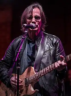 Musician Jackson Browne, playing an electric guitar and singing into a microphone.
