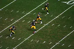 Four players run up the field as the kicker executes a kickoff