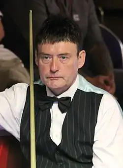 Jimmy White seated and holding his snooker cue.