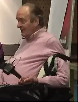This is a side-on mid-shot of Evans, sat in his wheelchair, wearing a pink jumper.