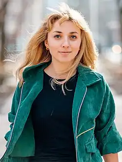 Kat Abughazaleh stands against a gray background looking directly at the viewer.