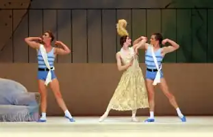 female dancer in long 1920s frock and feathered head-dress, with two male dancers dressed as athletes dancing on either side of her