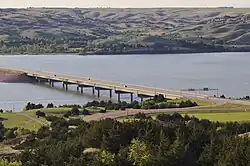 Distant view of a simple highway bridge crossing a wide river surrounded by rolling hills free of vegetation