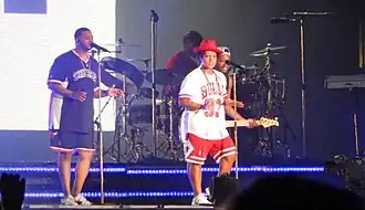 A picture of two men playing instruments and two singing into a microphone