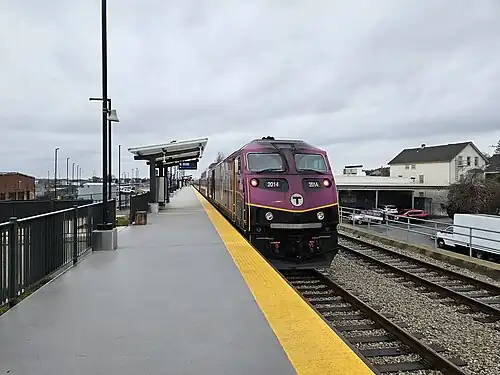 A diesel locomotive at a high-level railway platform in an urban area