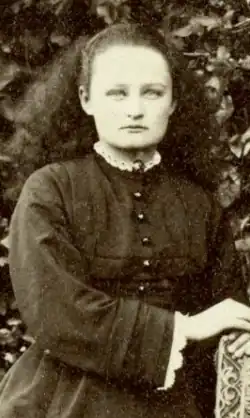 A white teenaged girl with long hair, wearing a dark dress