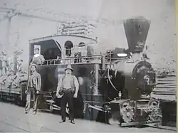 Men pose in front of an old steam engine.