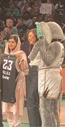 Malala Yousafzai with Clara Tsai and Ellie The Elephant at a New York Liberty game in September 2023. Malala is Holding a New York Liberty Jersey with her name on it.