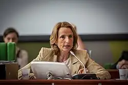 A blonde woman speaking at a meeting