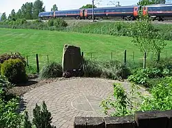 A circular garden with a plaque in the foreground, with an InterCity 225 travelling along the East Coast Main Line in the background