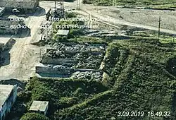 A waste dump between a gravel road and vegetation with gulls on top of it, shot from above