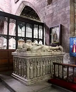 This image shows the monument to Sir Randal Brereton (d.1522) and his wife at St Oswald's, Malpas, Cheshire, representing a superb example of Tudor alabaster tomb sculpture. Two recumbent effigies lie side by side on top of an elaborate tomb chest, both figures carved in the traditional medieval manner with hands positioned in prayer and heads resting on pillows. The tomb chest below features an exceptional series of carved niches containing standing figures of saints, apostles, and other religious figures arranged between delicate Gothic columns under cusped arches, demonstrating the high quality of early sixteenth-century alabaster carving. The monument is positioned within the red sandstone Gothic architecture of the church, with a black wooden rood screen providing a dramatic backdrop. The effigies show fine attention to period costume and armour details, whilst the tomb chest's weeper figures create a rich sculptural narrative around the base. This monument exemplifies the continued use of medieval forms and iconography during the early Tudor period, before the religious changes of the Reformation transformed English monument design.RetryClaude can make mistakes. Please double-check responses.Research Sonnet 4