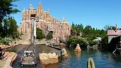 The splashdown drop out of Wild West Falls's artificial mountain; a boat loaded with passengers in the foreground courses the channel back to the station.