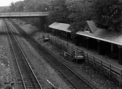 A two-track railway line in an open cut. At right is a platform several feet higher than track level, with a wooden canopy. Stairs lead from the platform down to track level.