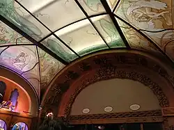 The arch above the south wall of the auditorium's entrance foyer, which lacks decorations. Above it is a glass ceiling with colorful decorations.