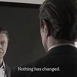 An image of David Bowie (view from the backside) looking at himself at the mirror.