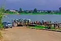 Bank of Oguta Lake showing human activities and rural dwellers. These include motorcyclists, loaded pontoon and automobile drivers engaged in movement of goods, services and people.