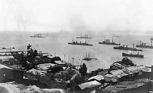 A group of large warships steaming slowly away from the city.
