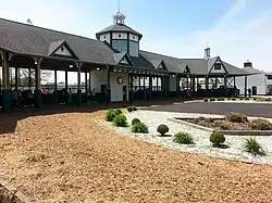 Paddock in background with blue sky and light clouds behind the paddock with mulch and rocks in the foreground with some shrubbery planted in the rocks