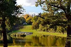 A colour photograph of a lake with a five-arch bridge in the middle distance below a tent on the hillside in the far distance
