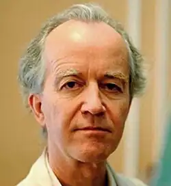 Three-quarter colour portrait of a clean-shaven, unsmiling man, with receding grey hair and strong features.