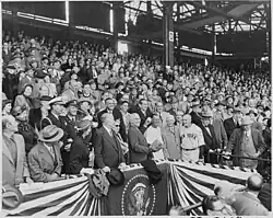 A wide shot with United States president Harry Truman in the center throwing a baseball.