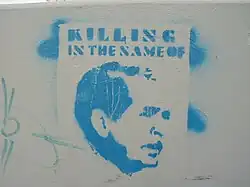 An image of George W. Bush stencilled in light blue with the words "Killing in the Name of" written above it.