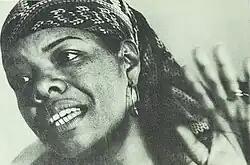 Black-and-white photograph of a African American woman in her forties, wearing a bandana and raising her left hand.