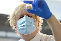 Johnson, wearing a facemask and surgical glove, examines a vial of vaccine