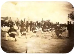 An old photograph showing a procession passing between lines of soldiers with tents in the background