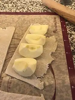 peeled, quartered apples lying on a piece of pastry crust