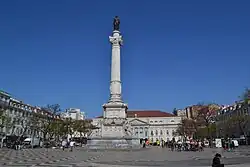 Photograph of a white stone column with a man wearing a laurel wreath and military dress and who holds forth a scrolled sheaf of paper on the top