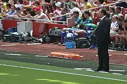 A coloured photograph of manager Rafael Benítez standing on the stadium touchline.
