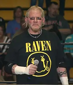 A color photograph of a man wearing a black t-shirt with yellow text and image