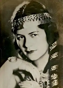 A young woman in a black and white 1930s headshot, with plaited hair interwoven with a metallic headdress