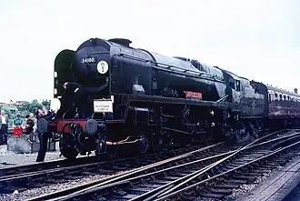 A posed side-and-front view of the rebuilt form of the locomotive. The locomotive is of conventional appearance, with a visible boiler and no flat covering plates. Smoke deflectors are fitted at the front of the locomotive.