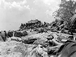 uneven beach in foreground littered with equipment, Marines, and amphibious vehicle in the distance