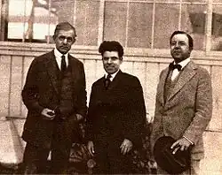 Three men standing wearing suits in front of a building