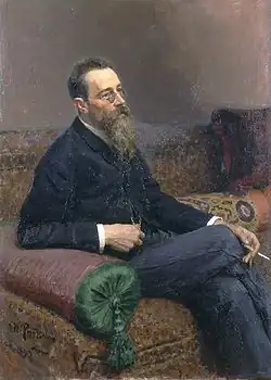 A man with glasses and a long beard sitting on a sofa, smoking.