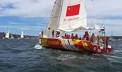 yellow, red and white boat in the middle of the blue sea with a red flag and people on it.