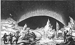 Full length picture of a man wearing heavy, Arctic clothing. He is standing outside in front of a snow-covered stack of wooden crates