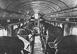 Grainy black-and-white image of single seats separated by the aisle, photographed from rear of plane facing cockpit