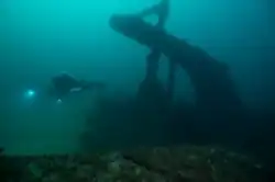 A scuba diver swims near a submerged ship's stern area.