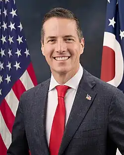 Official Senate portrait of Moreno smiling in front of the U.S. and Ohio flags, wearing a grey suit with American flag lapel pin, white shirt, and red tie.
