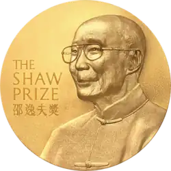 A gold circular medal with a depiction of an elderly man with glasses wearing a jacket buttoned to the neck; the English words "The Shaw Prize" and Chinese characters "邵逸夫獎" engraved on it