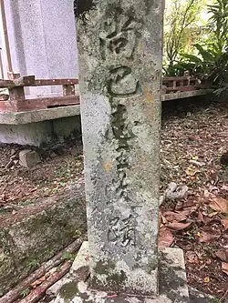 A stone stele bearing an inscription in a forested environment