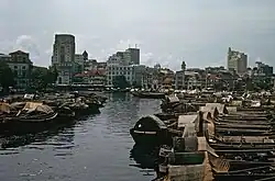 A river with many moored boats and a city skyline beyond